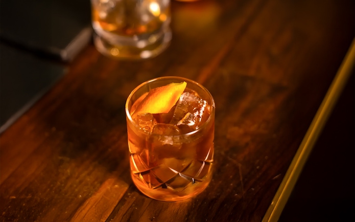 Jameson whiskey cocktail with orange peel garnish on a wooden table.