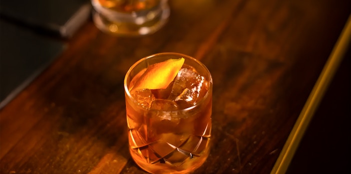 Jameson whiskey cocktail with orange peel garnish on a wooden table.