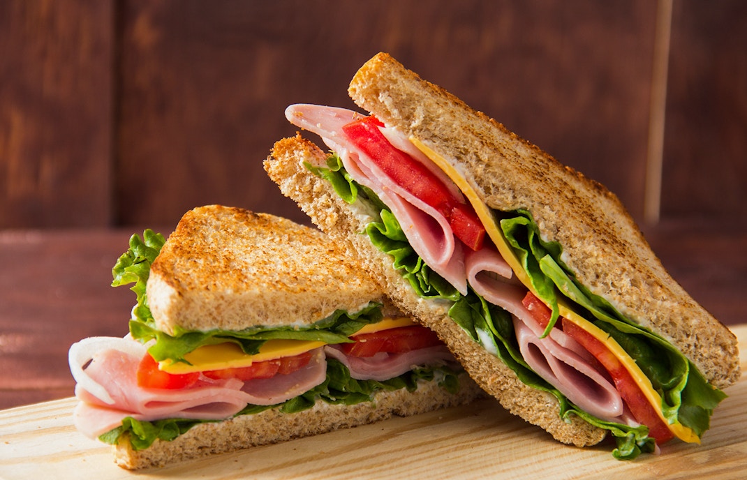 Ham and cheese sandwich with lettuce and tomato on whole grain bread.