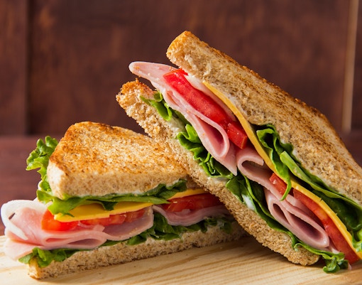 Ham and cheese sandwich with lettuce and tomato on whole grain bread.