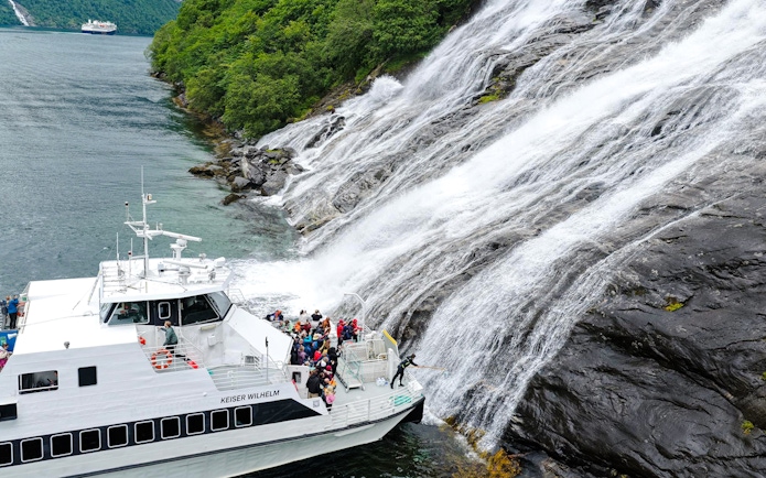 Boat with people near the Bachelor Waterfall in Geiranger Fjord, Norway.
