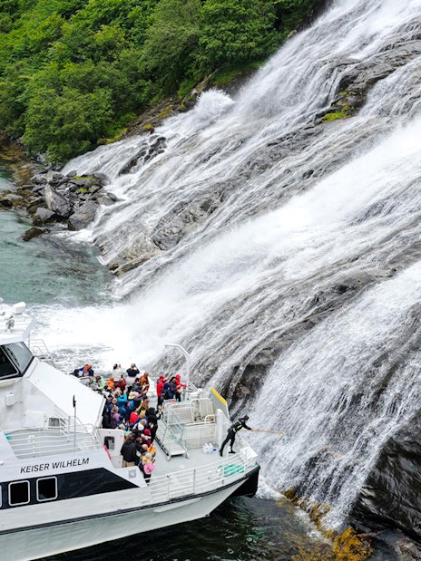 Boat with people near the Bachelor Waterfall in Geiranger Fjord, Norway.
