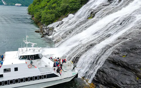 Boat with people near the Bachelor Waterfall in Geiranger Fjord, Norway.