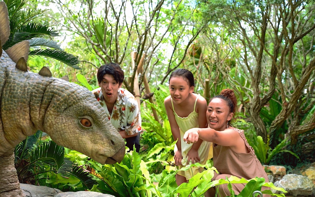 Visitors interacting with a dinosaur exhibit at JUNGLIA OKINAWA Park.
