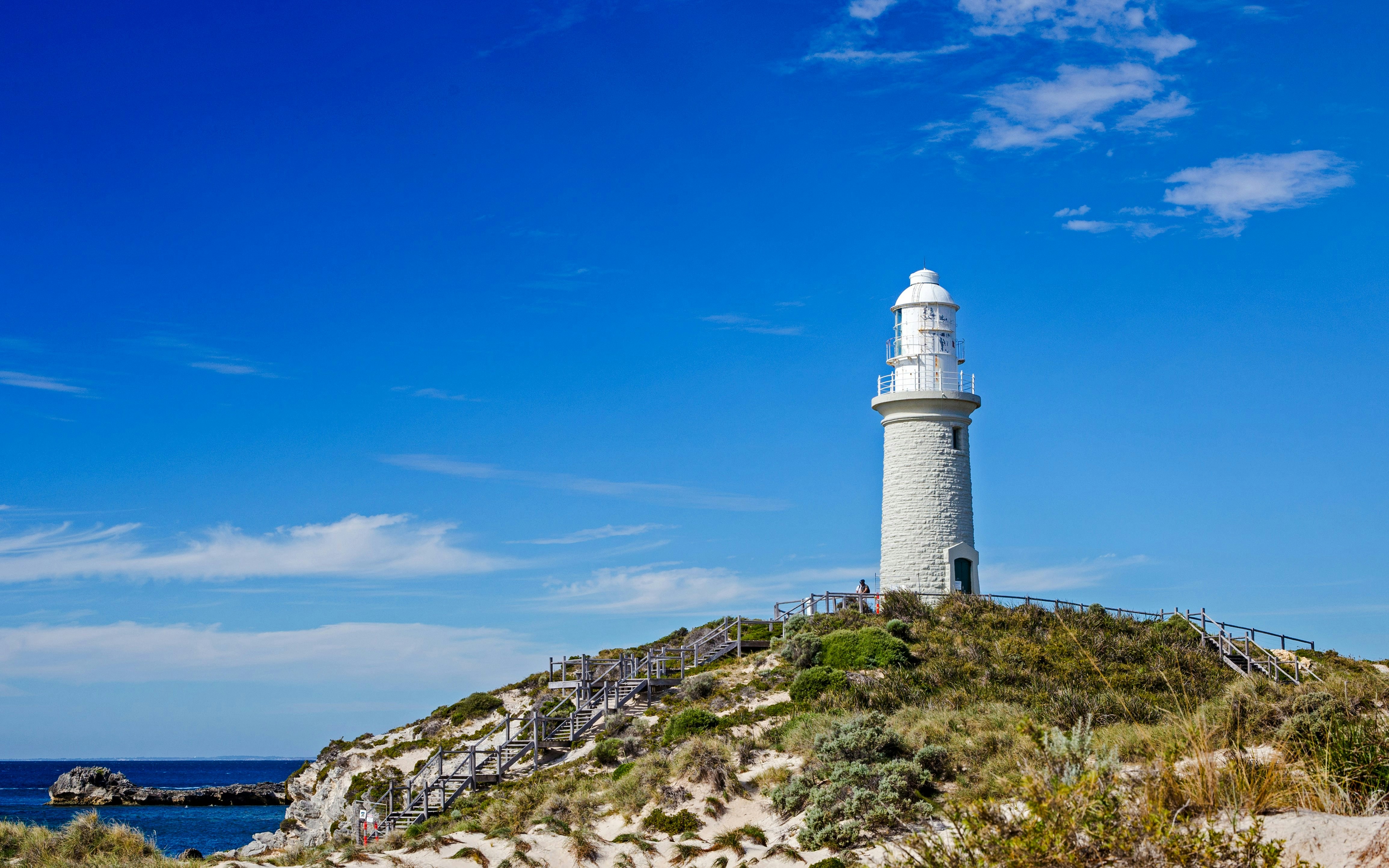 Bathurst Lighthouse on Rottnest Island with clear blue sky and coastal vegetation.