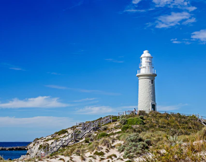 Bathurst Lighthouse on Rottnest Island with clear blue sky and coastal vegetation.