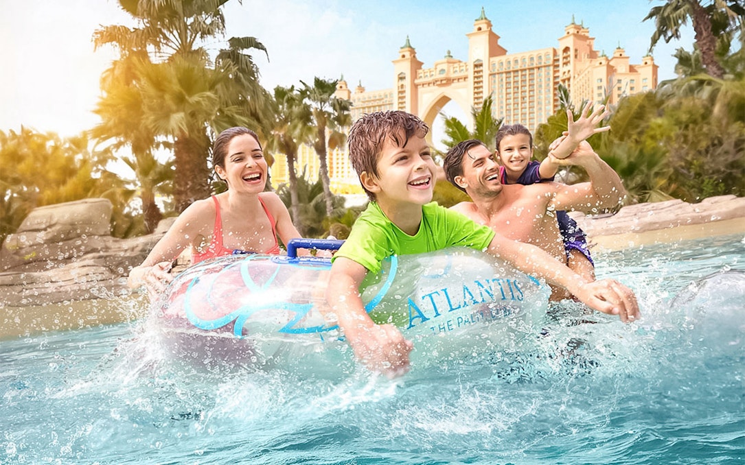 Family enjoying water ride at Atlantis The Palm with iconic hotel in background.