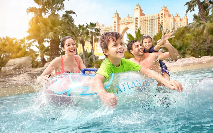 Family enjoying water ride at Atlantis The Palm with iconic hotel in background.