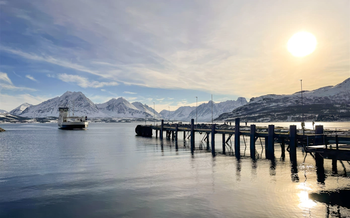 Ferry docked near snowy mountains and pier in Tromsø, Lyngen Alps.