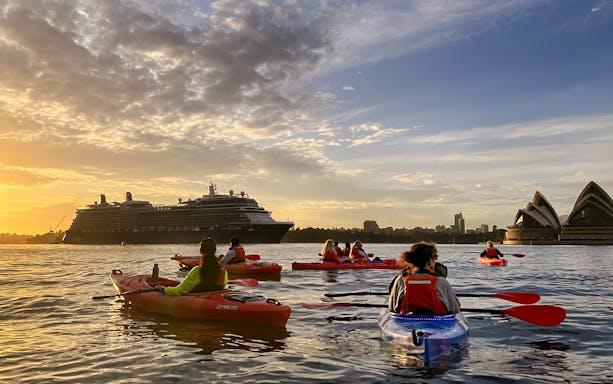 Kayakers on Sydney Harbour at sunrise near the Opera House and cruise ship.