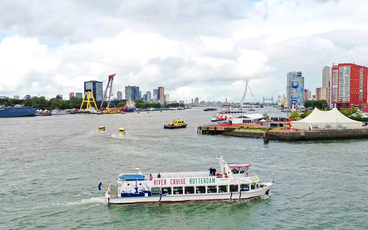 Rotterdam river cruise boat on the water with city skyline and Erasmus Bridge in the background.
