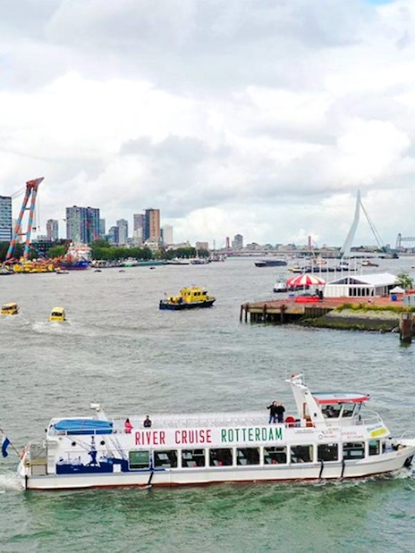 Rotterdam river cruise boat on the water with city skyline and Erasmus Bridge in the background.