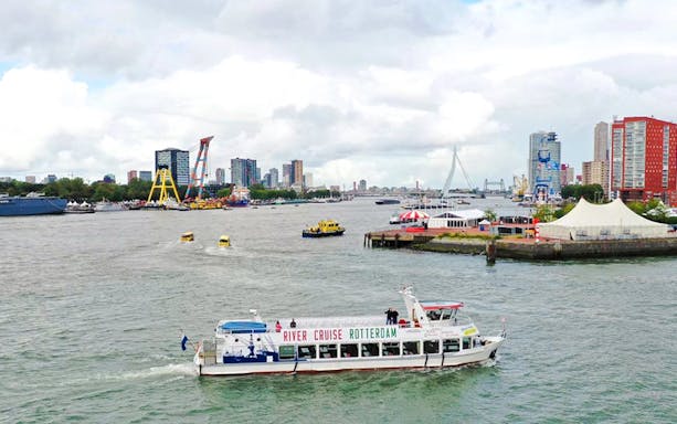 Rotterdam river cruise boat on the water with city skyline and Erasmus Bridge in the background.