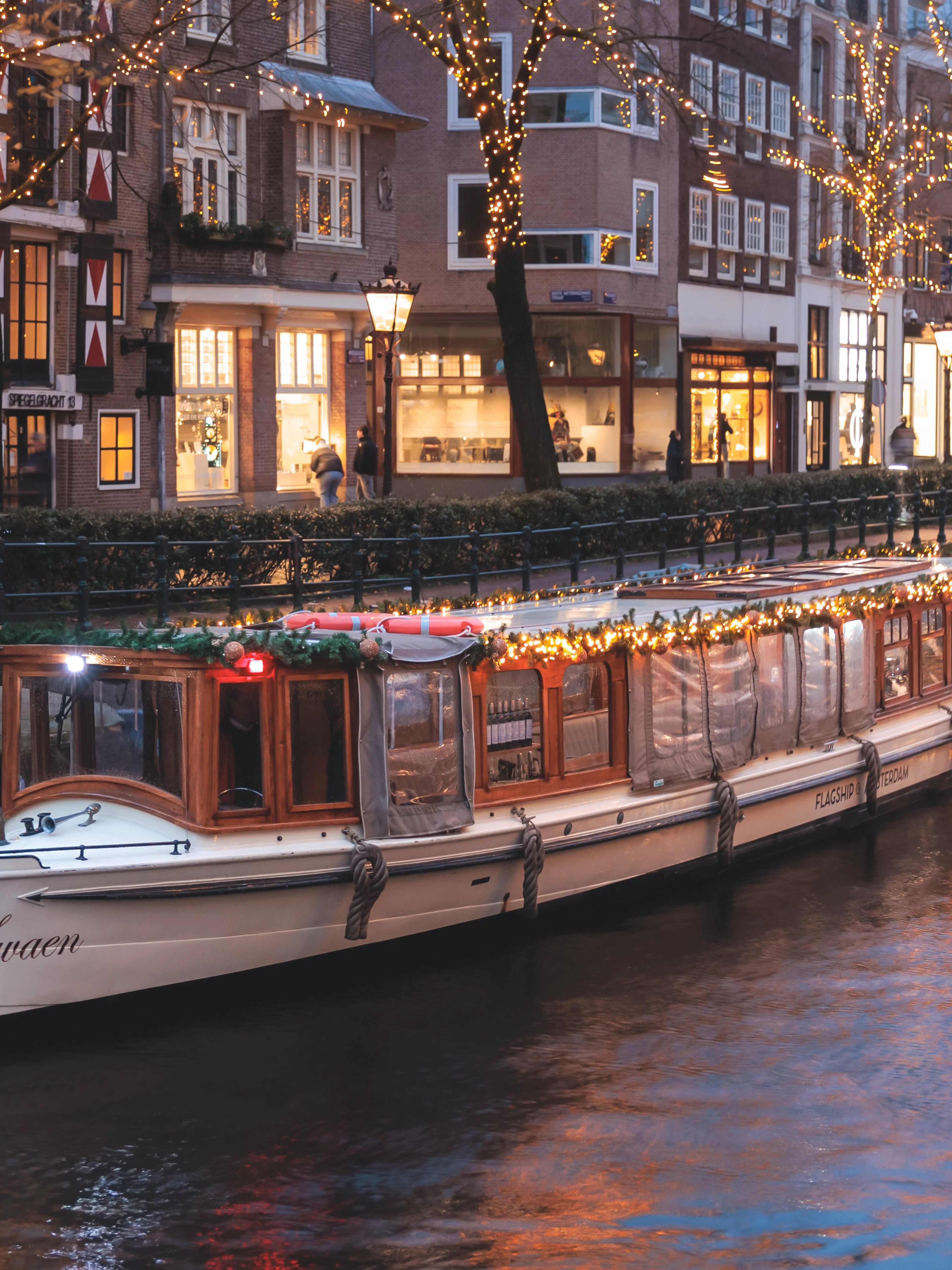 Luxury saloon boat adorned with lights cruising Amsterdam canal at dusk.