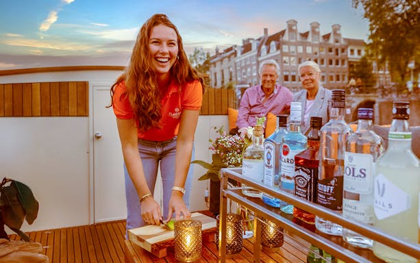 Bar on Amsterdam canal boat with drinks and bartender preparing lime slices.