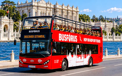Open-top tour bus near Dolmabahçe Palace, Istanbul, with passengers enjoying the Bosphorus view.