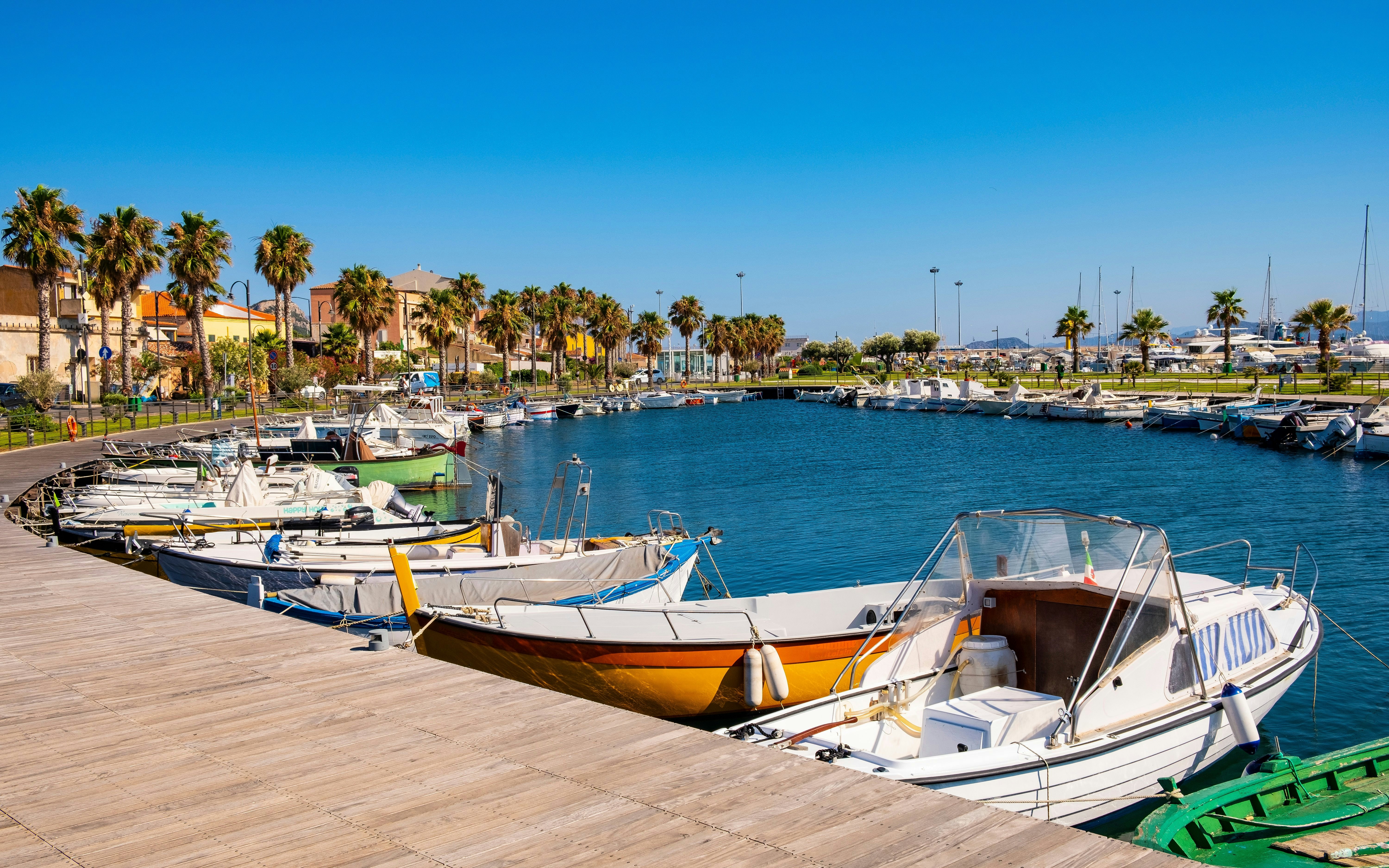Boats docked at Golfo Aranci Marina with palm trees and waterfront promenade.