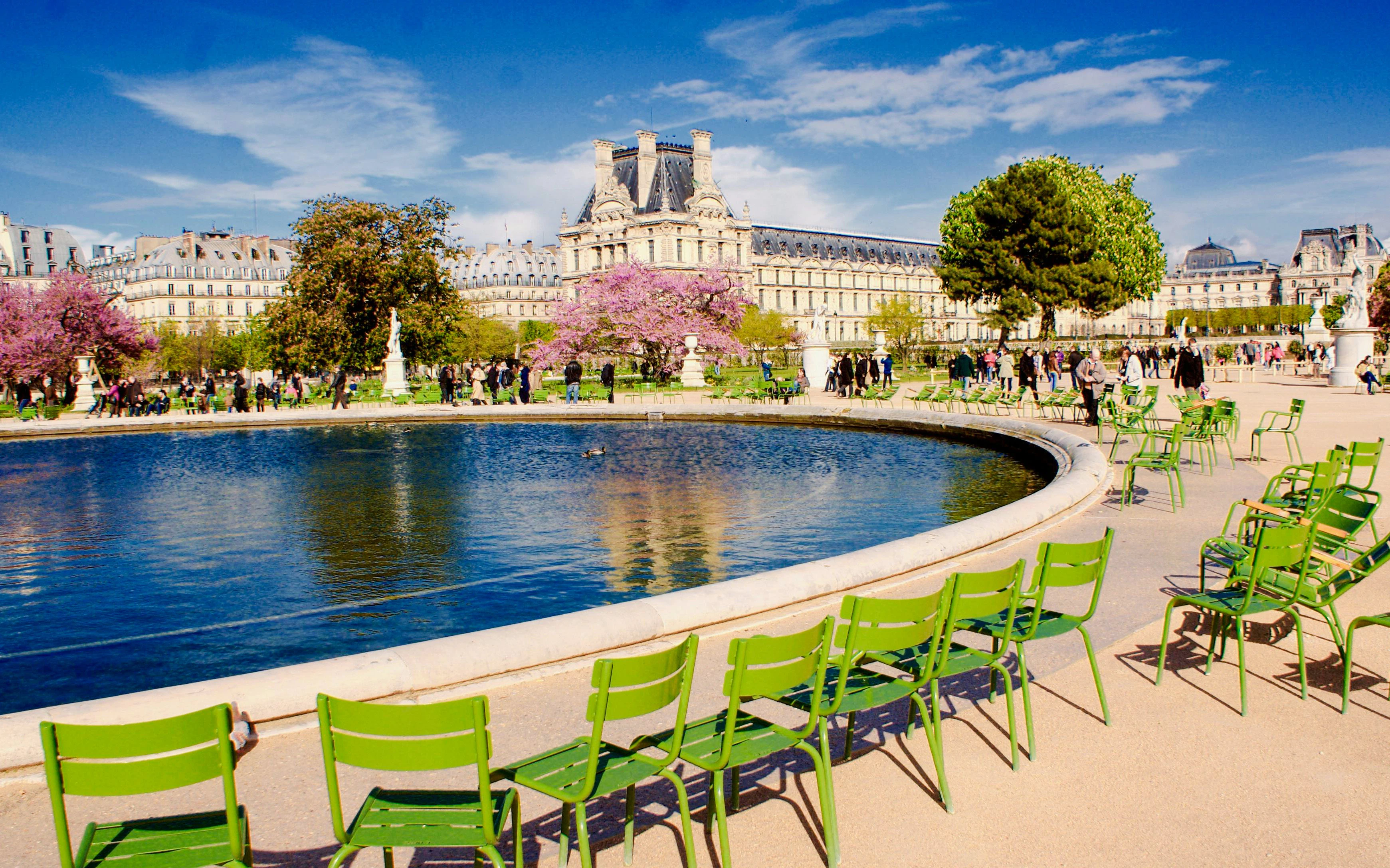 Tuileries Garden central basin with green chairs and Louvre in background, Paris.