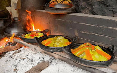 Traditional tajine cooking over open fire with vegetables in clay pots.