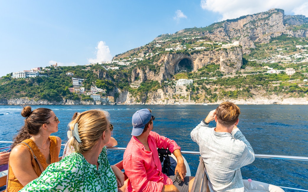 Tourists on a boat viewing cliffs and buildings along the Amalfi Coast near Positano.