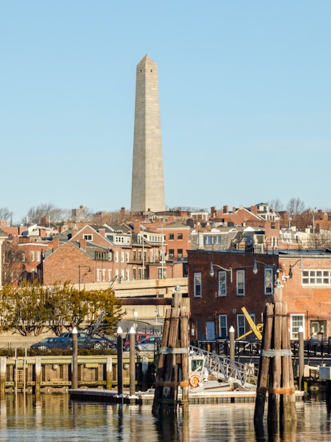 Bunker Hill Monument viewed from the harbor with historic brick buildings in Boston.