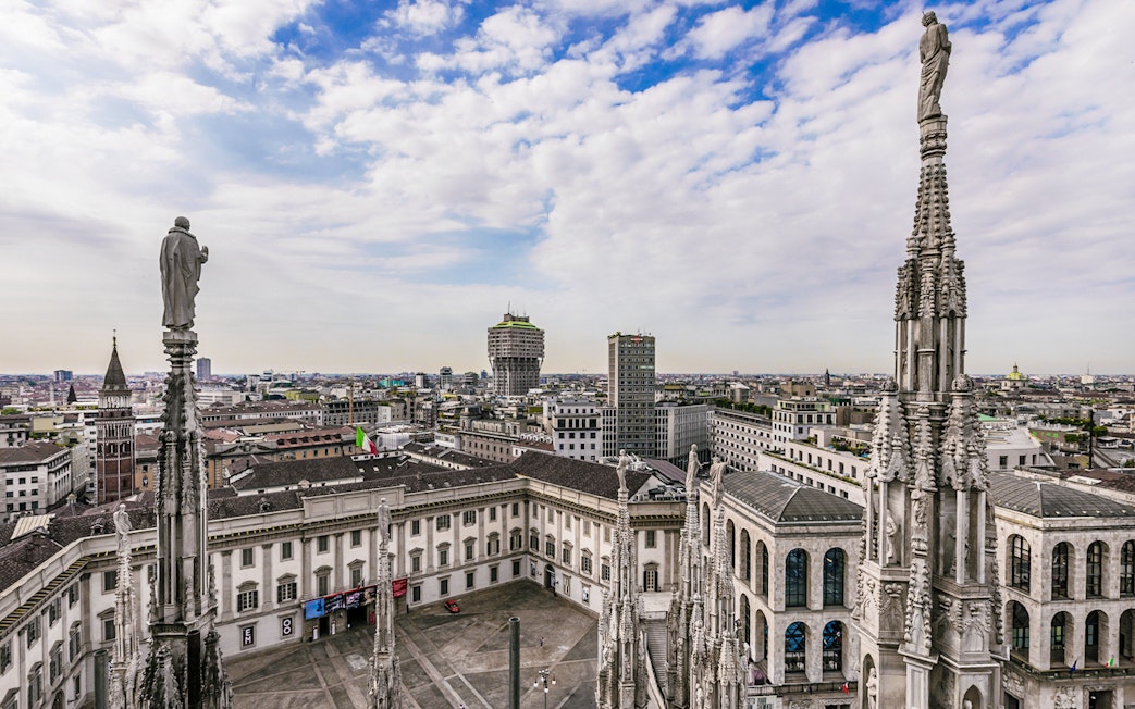 Aerial view of Milan cityscape from Duomo Cathedral rooftop, featuring spires and historic buildings.
