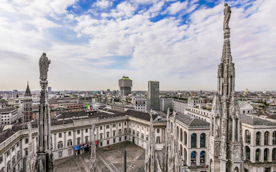 Aerial view of Milan cityscape from Duomo Cathedral rooftop, featuring spires and historic buildings.
