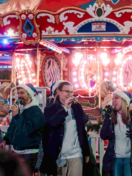 Singers performing at Winter Glow festival in front of a carousel at Sankofa Square.