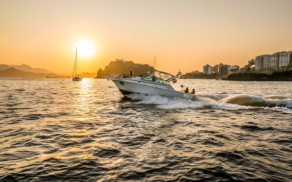 Tourists on a boat during Rio de Janeiro sunset cruise with city skyline in background.