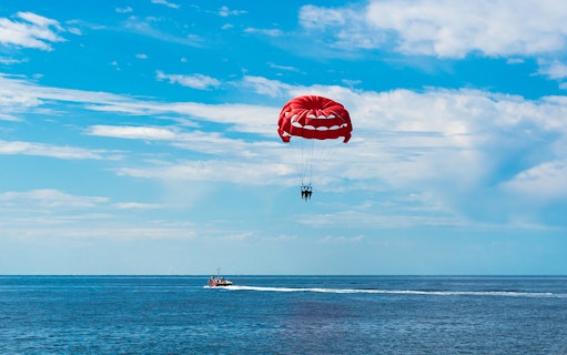 Parasailing over the ocean in Albufeira with a red parachute.