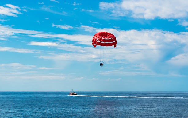 Parasailing over the ocean in Albufeira with a red parachute.