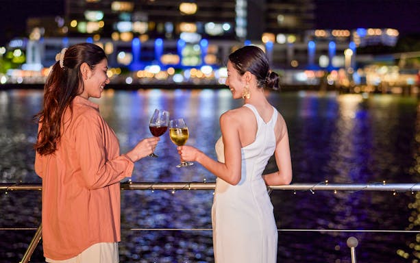 Two women toasting with wine on Spirit of Cairns dinner cruise at night, Australia.