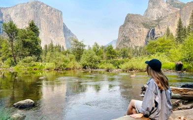 Visitor sitting by Merced River with El Capitan view, Yosemite National Park, California.