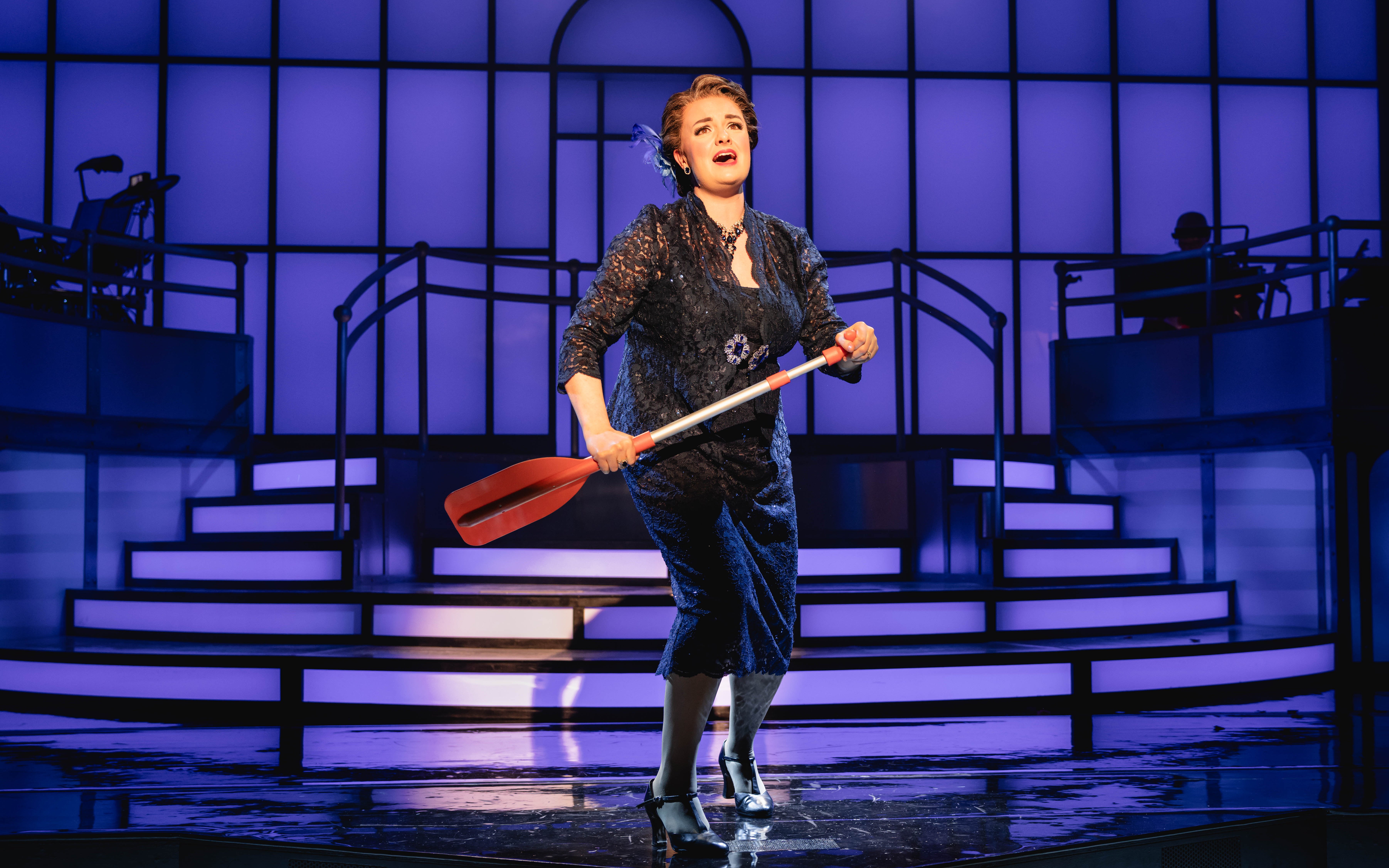 Performer on stage during Titanique Westend show holding a red oar.