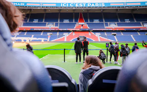 Visitors touring PSG Stadium in Paris, France, viewing the field and stands.