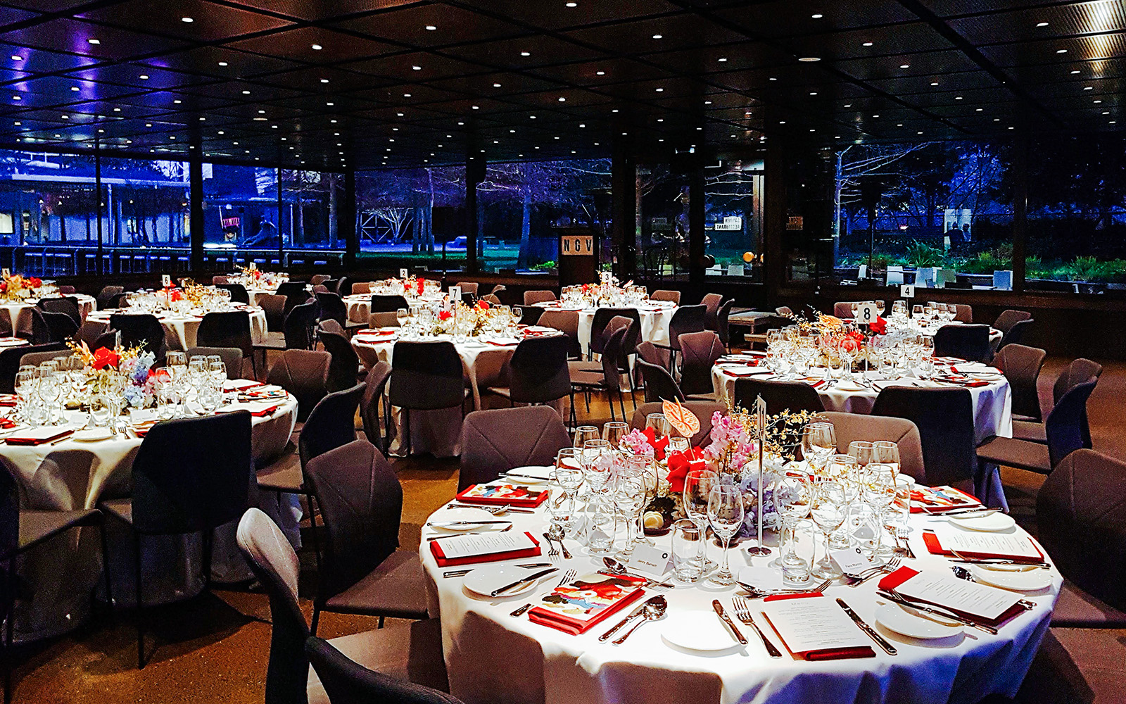 NGV garden restaurant interior with tables set for dinner, featuring floral centerpieces.