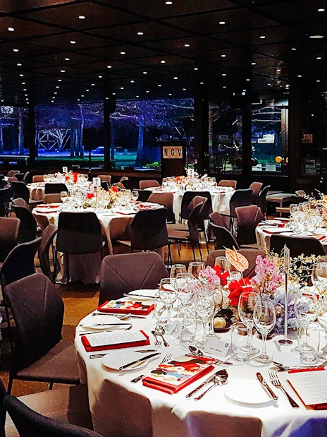 NGV garden restaurant interior with tables set for dinner, featuring floral centerpieces.