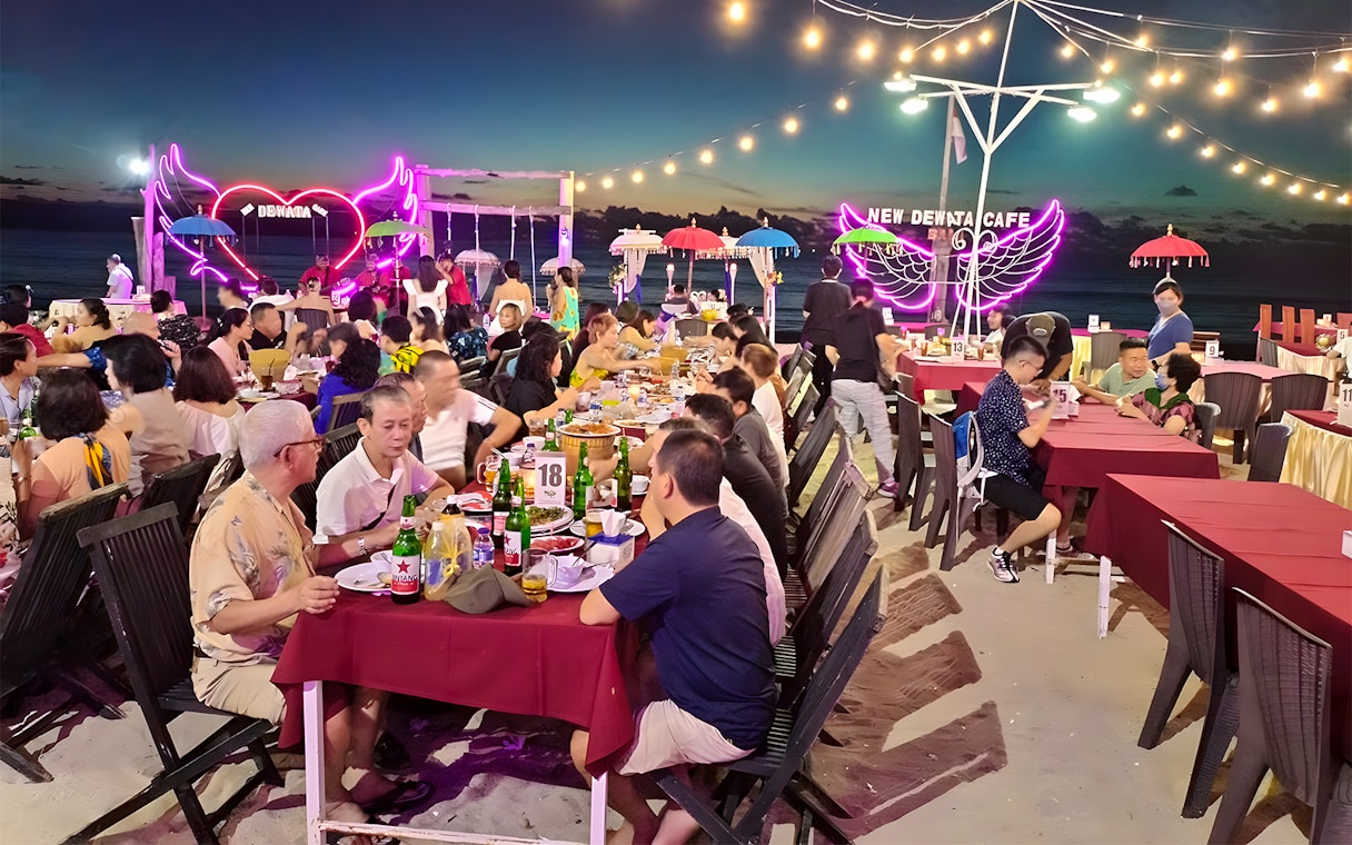 Dining at a beachfront seafood restaurant in Jimbaran, Bali with neon lights and ocean view.