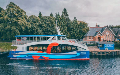 Loch Ness cruise boat docked near a historic building with trees in the background.