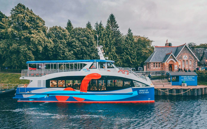 Loch Ness cruise boat docked near a historic building with trees in the background.