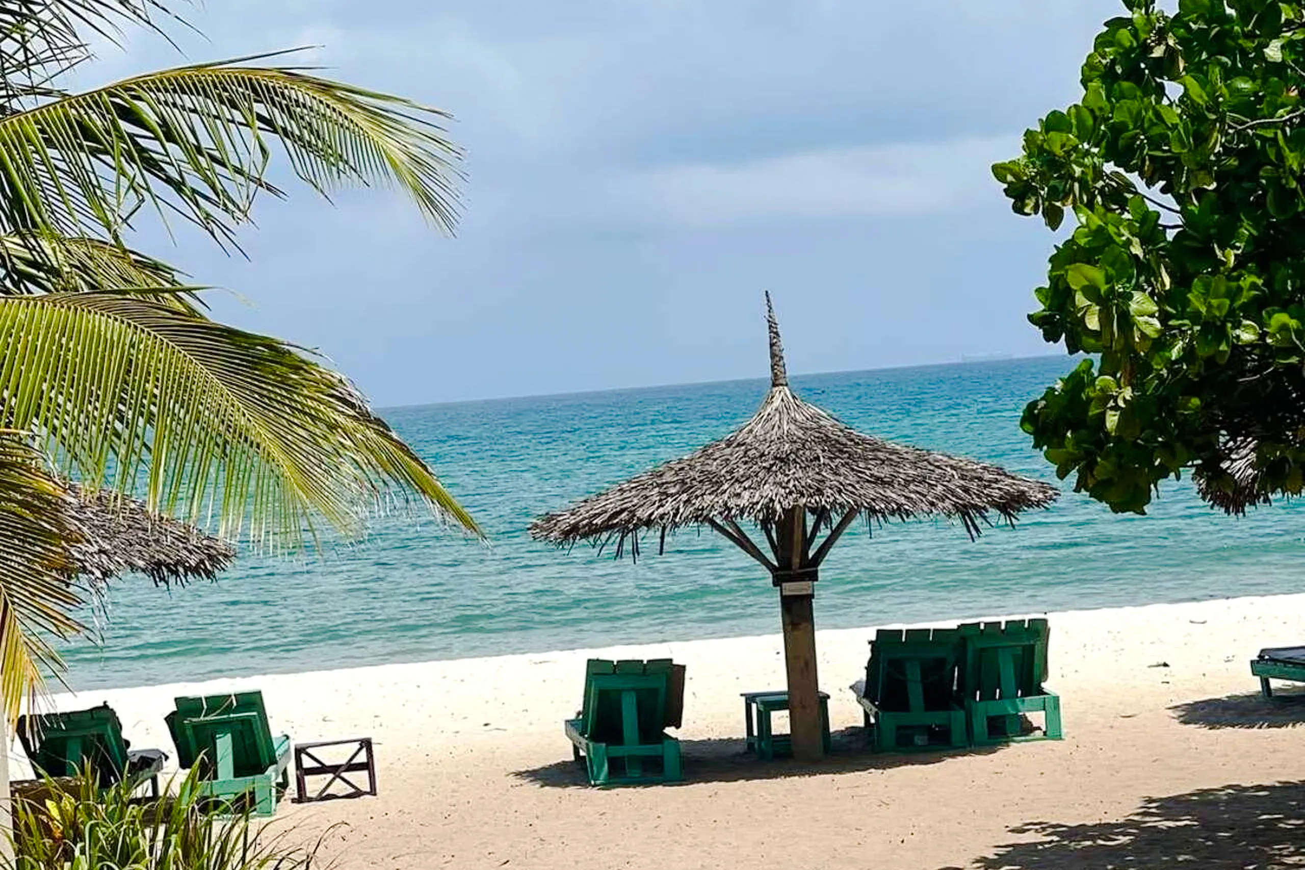 Beachfront with palm trees and lounge chairs under a thatched umbrella, Dar es Salaam, Zanzibar.