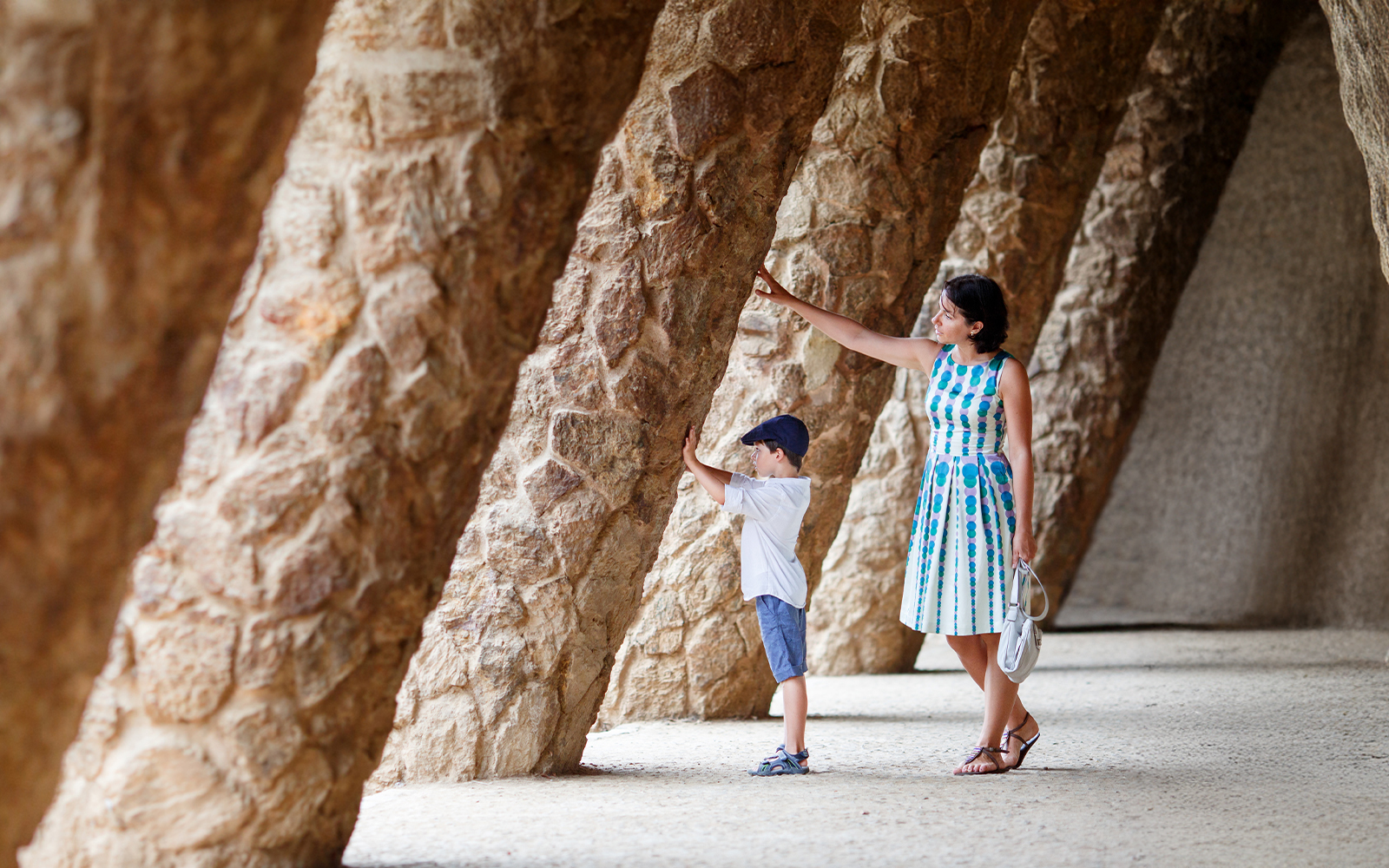 Mother and son exploring stone columns in Park Guell, Barcelona.