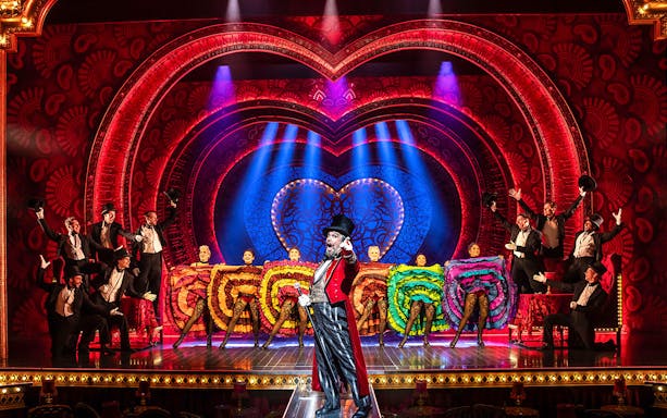 Performers on stage at MOULIN ROUGE! De Musical with vibrant costumes and elaborate set design.