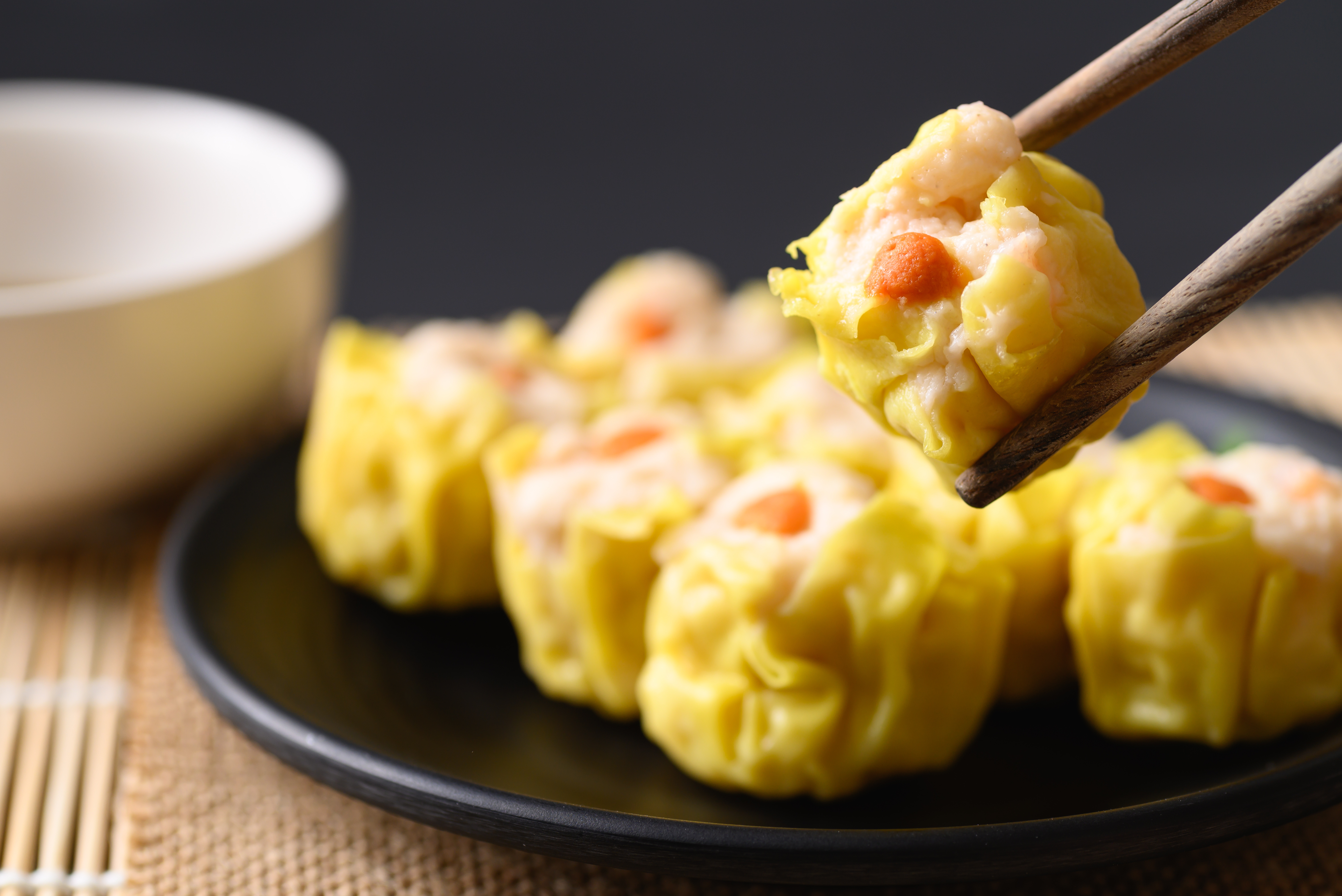 Shrimp shumai dumplings on a black plate, one held with chopsticks.