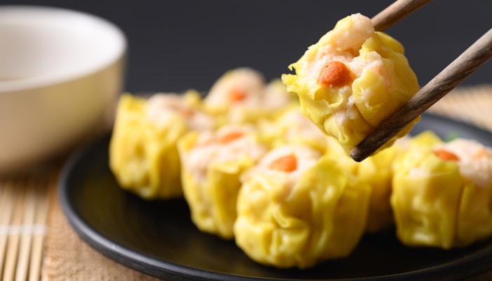 Shrimp shumai dumplings on a black plate, one held with chopsticks.