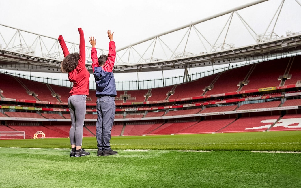 Visitors raising arms on Arsenal FC Emirates Stadium field during tour.