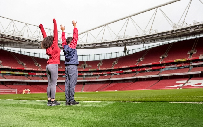 Visitors raising arms on Arsenal FC Emirates Stadium field during tour.