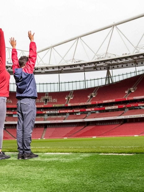 Visitors raising arms on Arsenal FC Emirates Stadium field during tour.