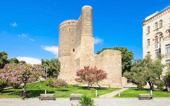 Maiden Tower in Baku surrounded by trees and flowers on a sunny day.
