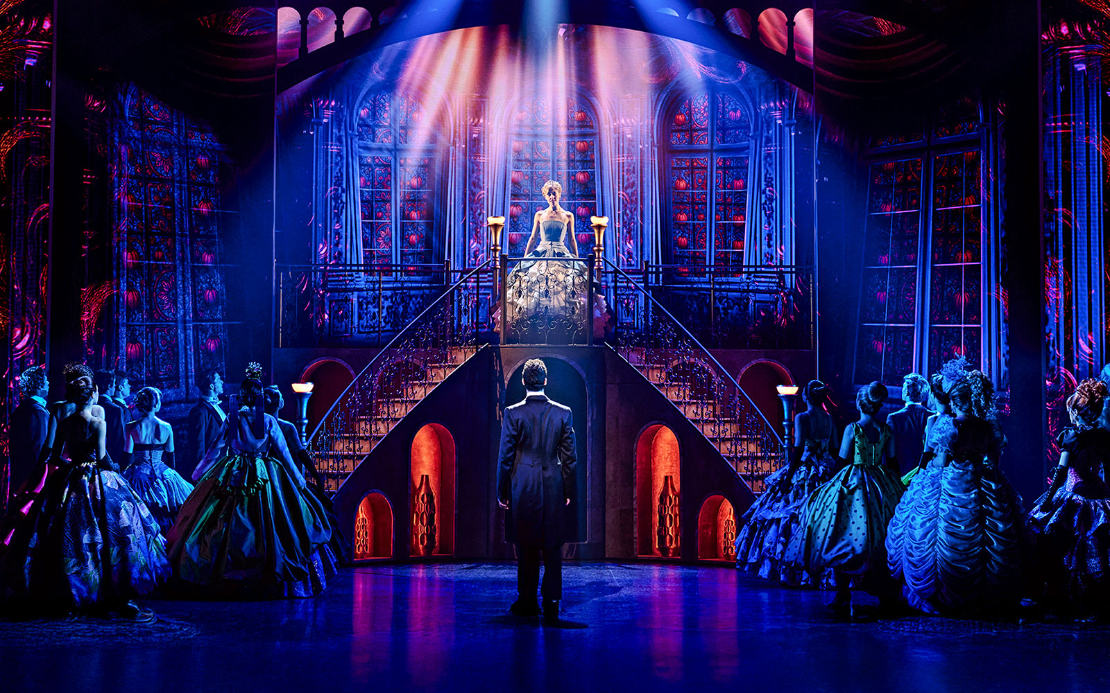 Cinderella on stage at Madrid theater, standing on staircase, surrounded by cast in elegant costumes.